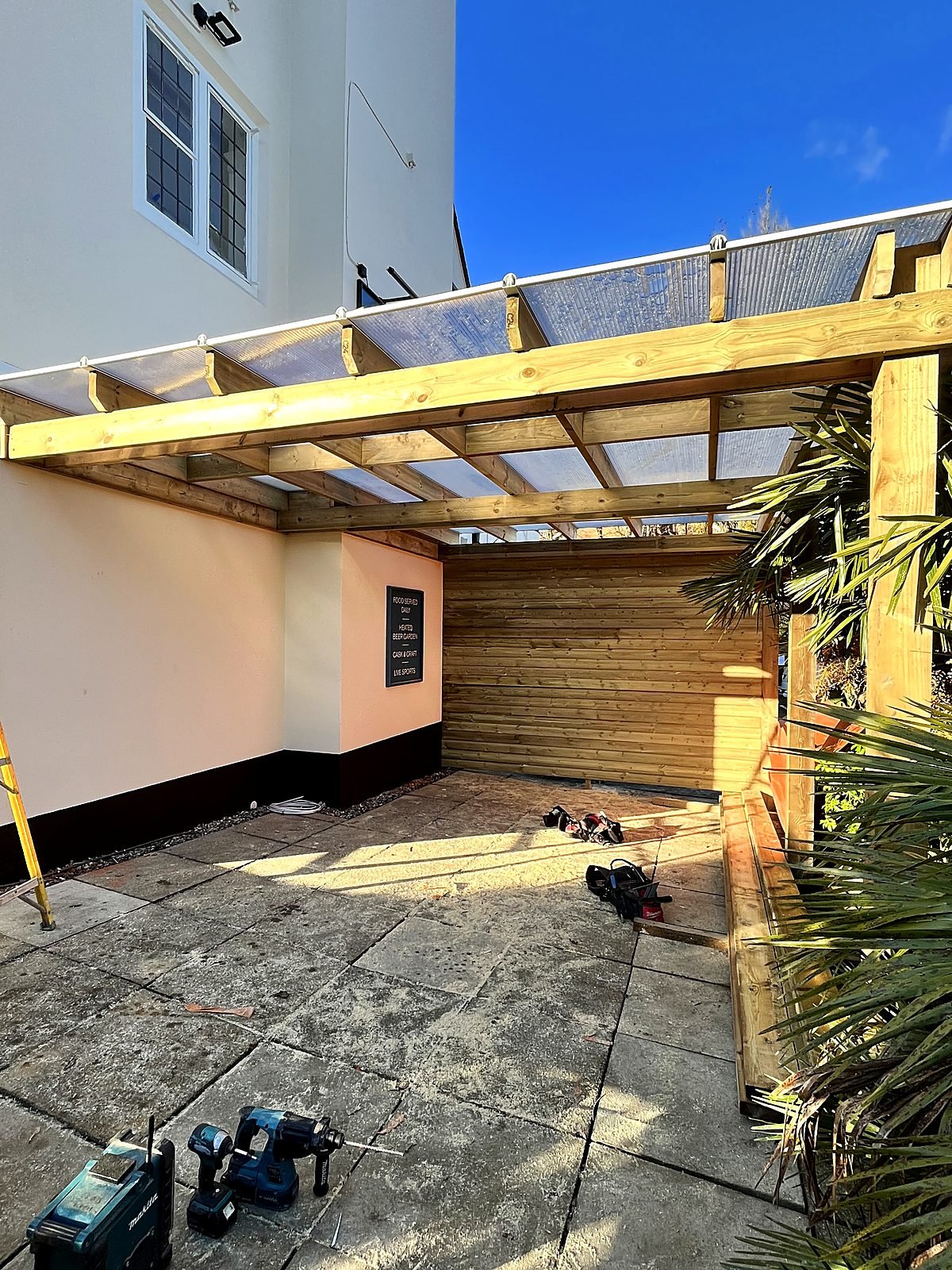 Heated beer garden canopy at a pub — treated timber frame with a polycarbonate roof and cladded back wall